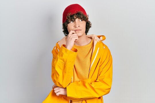 Handsome young man wearing yellow raincoat serious face thinking about question with hand on chin, thoughtful about confusing idea