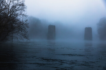 Heavy fog over the lake with a bridge columns in the water