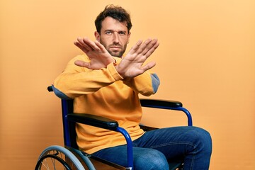 Handsome man with beard sitting on wheelchair rejection expression crossing arms doing negative sign, angry face