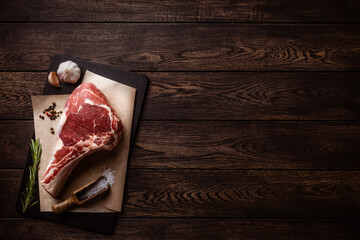 Raw tomahawk or cowboy beef steak on cutting board over wooden background with copy space
