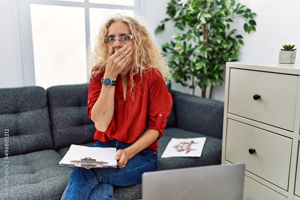 Poster Middle age psychologist woman at consultation office shocked covering mouth with hands for mistake. secret concept.