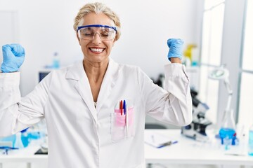 Middle age blonde woman working at scientist laboratory celebrating mad and crazy for success with...