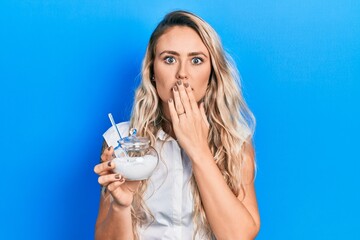 Beautiful young blonde woman holding bowl with sugar covering mouth with hand, shocked and afraid...