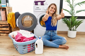 Young beautiful woman doing laundry sitting by wicker basket approving doing positive gesture with...