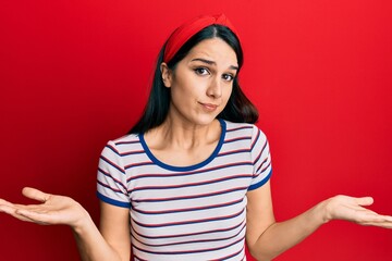 Young hispanic woman wearing casual clothes clueless and confused expression with arms and hands raised. doubt concept.