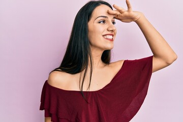 Young hispanic woman wearing casual clothes very happy and smiling looking far away with hand over head. searching concept.