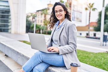 Young hispanic woman executive using laptop sitting on bench at street