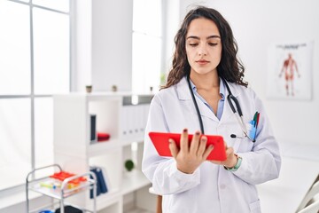 Young hispanic woman wearing doctor uniform using touchpad at clinic