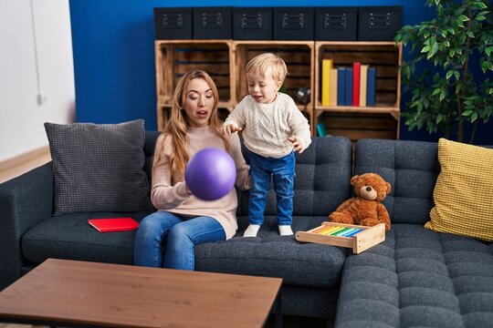 Mother and son playing with ball sitting on sofa at home
