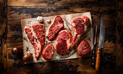 Assortment of raw meat cut with seasoning and utensils on wooden rustic board