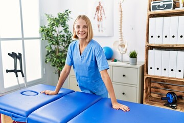 Young blonde woman wearing physiotherapist uniform standing at rehab clinic