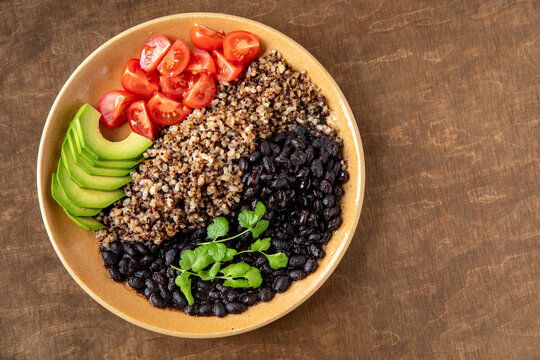 Vegan bowl with cooked beans, grains (brown rice, barley, quinoa) and raw vegetables (coriander, avocado, tomato). Top view.
