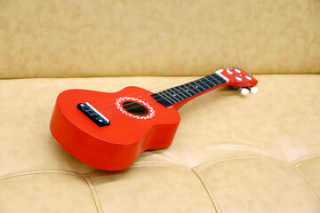 Red ukulele on a leather sofa. Small guitar in classic style