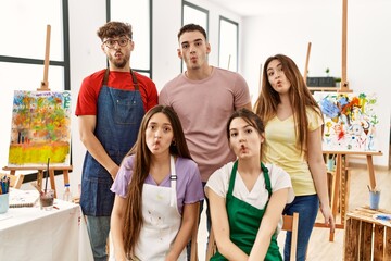 Group of five hispanic artists at art studio making fish face with lips, crazy and comical gesture. funny expression.