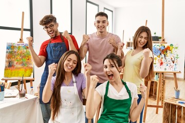 Group of five hispanic artists at art studio very happy and excited doing winner gesture with arms raised, smiling and screaming for success. celebration concept.