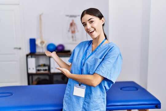 Young hispanic woman wearing physiotherapist uniform standing at clinic inviting to enter smiling natural with open hand