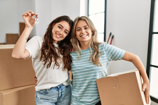 Young beautiful couple smiling happy holding cardboard box and key of new home.