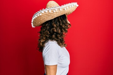 Middle age hispanic woman holding mexican hat looking to side, relax profile pose with natural face with confident smile.