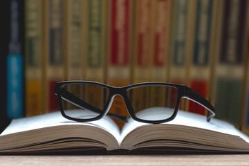 Eyeglasses lie on an open book in the background of the library. Reading Glasses. Classic black...