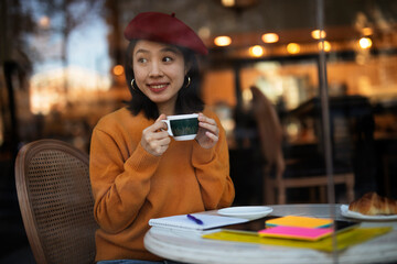 Beautiful Chinese woman drinking coffee in cafe. Young smiling woman enjoy in restaurant..