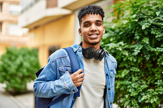 Hispanic young man smiling wearing headphones at the street
