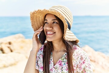 Young latin girl wearing summer hat talking on the smartphone at the beach.