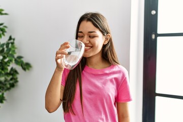 Young latin woman smiling confident drinking water at home