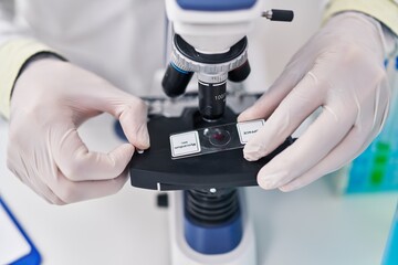 Young hispanic man wearing scientist uniform using microscope at laboratory