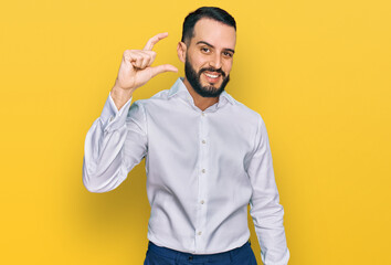 Young man with beard wearing business shirt smiling and confident gesturing with hand doing small size sign with fingers looking and the camera. measure concept.