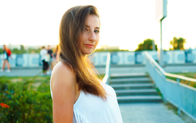 Beautiful young woman with long hair walks around city against backdrop of sunset. Hello spring.