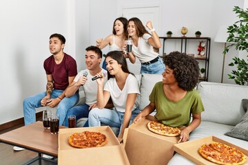 Group of young friends having party eating italian pizza and singing song at home.