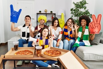 Group of young people wearing team scarf cheering football game doing ok sign with fingers, smiling friendly gesturing excellent symbol