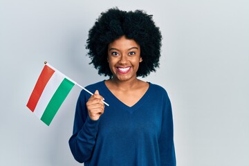Young african american woman holding hungary flag looking positive and happy standing and smiling with a confident smile showing teeth