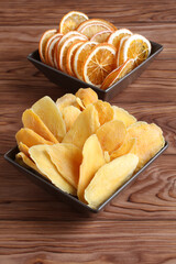 Dried pieces of mango and orange lying on a brown ceramic bowls on a wooden table. Macro. Closeup
