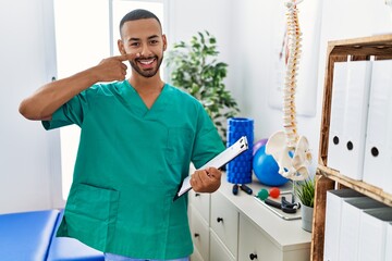 African american physiotherapist man working at pain recovery clinic pointing with hand finger to face and nose, smiling cheerful. beauty concept