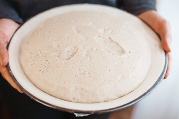 Bowl with yeast dough in hands, close-up. Cooking homemade bread or pizza.