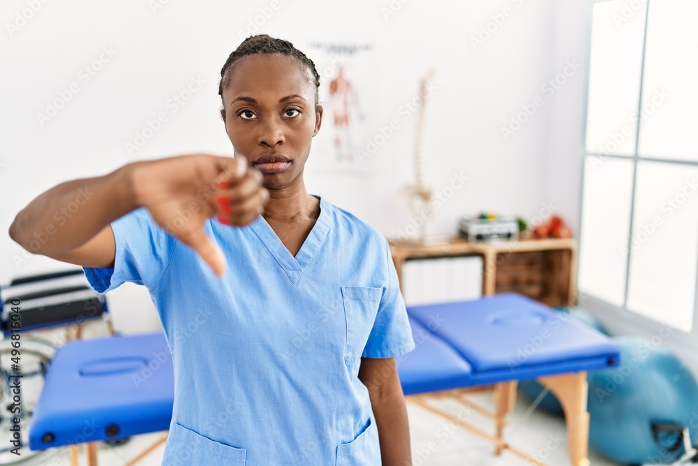 Sticker Black woman with braids working at pain recovery clinic looking unhappy and angry showing rejection and negative with thumbs down gesture. bad expression.