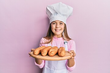 Beautiful brunette little girl wearing baker uniform holding homemade bread celebrating crazy and amazed for success with open eyes screaming excited.