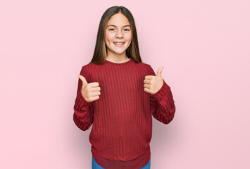 Beautiful brunette little girl wearing casual sweater success sign doing positive gesture with hand, thumbs up smiling and happy. cheerful expression and winner gesture.