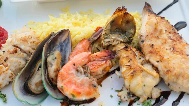 Close-up of sea food platter with charcoal grilled shrimps, cooked mussels, squid and fish fillet with fried rice. Set of delicious mixed seafood for lunch on white plate on restaurant table. Top view
