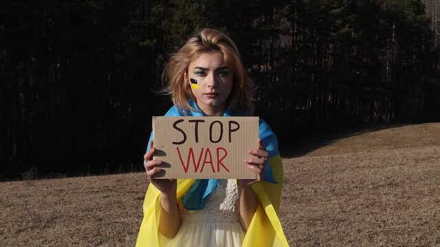 Stop War! Woman with protest sign. National symbol of Ukraine. Lady with blood makeup hold patriotic nameplate. Stand with Ukraine, support and solidarity. No war!
