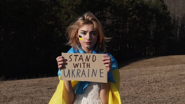 Stand with Ukraine! Stop War! Woman with protest sign. National symbol of Ukraine. Lady with blood makeup hold patriotic nameplate. Stand with Ukraine, support and solidarity. No war!