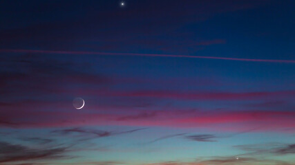 Crescent young Moon and planets on colorful sky.