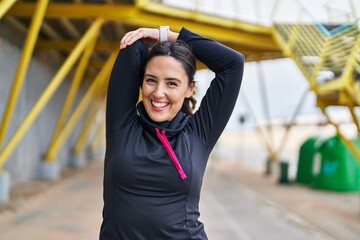 Young hispanic woman wearing sportswear stretching arms at street