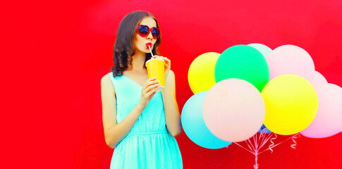Obraz na płótnie Canvas Beautiful young woman drinking juice with colorful balloons on red background, blank copy space for advertising text