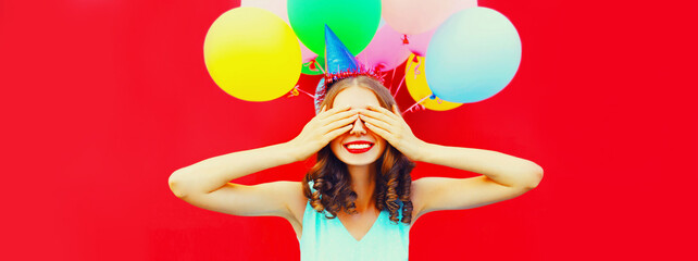 Portrait of happy surprised woman making wish covering her eyes with hands in birthday hat on...