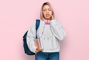 Hispanic woman with pink hair wearing student backpack and headphones touching mouth with hand with...
