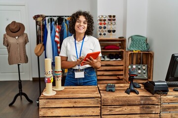 Young latin shopkeeper woman using touchpad working at clothing store. - obrazy, fototapety, plakaty