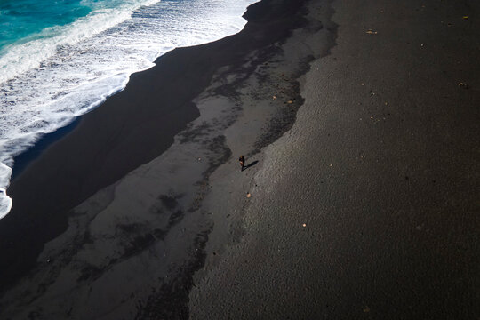 Aerial view of a person walking along the coastline on a black sand beach near El Lago Verde (Green Lake) in Lanzarote, Canary Islands, Spain.