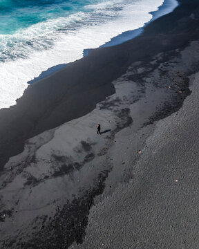 Aerial view of a person walking along the coastline on a black sand beach near El Lago Verde (Green Lake) in Lanzarote, Canary Islands, Spain.